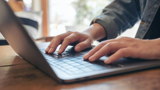 Closeup image of woman's hands using and typing on laptop keyboard on the table