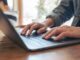 Closeup image of woman's hands using and typing on laptop keyboard on the table