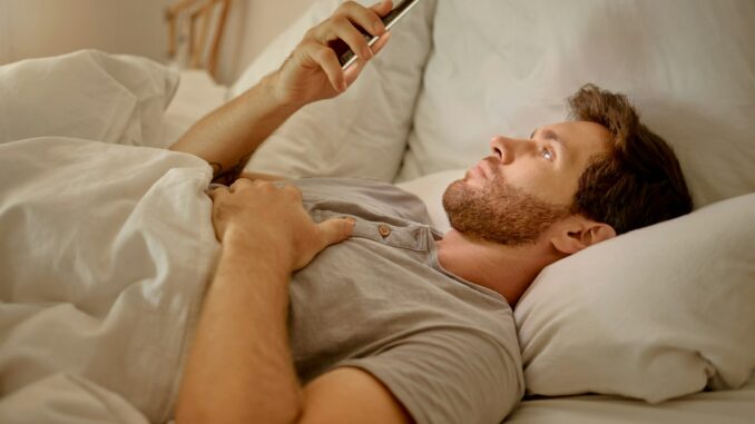 Man in bed at night with phone live streaming on mobile app, social media content on the internet