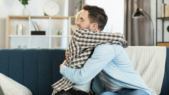 Same sex couple sitting on couch in strong hugs